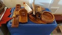Overhead photo showing various wood art and decoration items placed on a blue plastic container, various carved wood pieces including trays, bowls, plaques, and scoops.