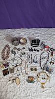Wide view of the lot on white textured surface showing assorted necklaces, earrings, bangles, and pins including pearls, butterflies, and other motifs.