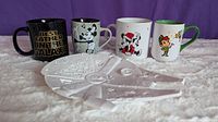 Front view of 4 Disney mugs (Best Father in the Galaxy, Steamboat Willie Mickey, Christmas Minnie and Mickey, Peter Pan) and the white Millennium Falcon dish in front.