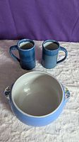 Front view showing two deep blue handmade mugs behind a wide blue Hall's bowl with floral handles.