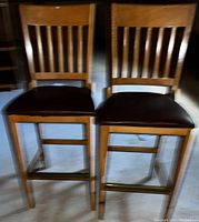 Two wooden bar chairs with slat backs and brown cushioned seats, footrests with brass bars visible.