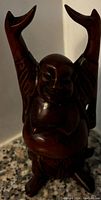 Single wooden carved Buddha statue with arms raised, showing dark polished finish and smiling facial expression.