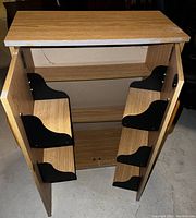 Photo shows oak utility cabinet with two open doors, interior shelves, and black metal brackets inside. Visible scratches on wood surfaces.