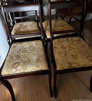 Four vintage wooden dining chairs with dark finish and floral patterned upholstered seats arranged closely together on hardwood floor.