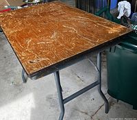 Photo showing the wood tabletop with scratches and metal folding legs.