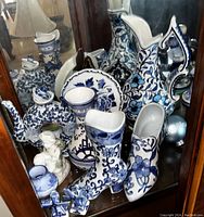 Display of Delft blue and white porcelain including ceramic horse, shoes, jugs, and small containers with floral patterns.