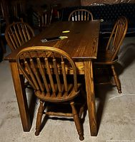 Photo of rectangular wooden Windsor dining table and four matching Windsor chairs arranged around it, showing wood grain details and classic spindle backs.