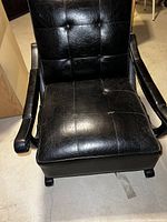 Front view of a black executive chair showing cushioned seat and backrest with tufted design and armrests. Scratches and wear are visible on the upholstery.