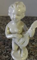 Glossy ceramic cherub figurine playing a guitar with detailed sculpting