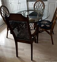 Round glass top dining table with four lattice-backed wooden chairs around it, cushions with floral upholstery visible.