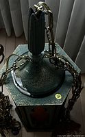 Close-up of dark green hexagonal pendant lamp top with attached chain showing signs of wear and scratches.