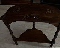 Dark mohohany wood Victorian style console side table with decorative carvings on top, curved edges, and turned wooden legs supporting a lower shelf.