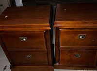 Photo of two oak night tables side by side showing front and top surfaces in medium brown finish with two drawers each and metal ring pull hardware.
