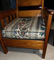 Photo showing the front side of an antique mission oak chair with vertical slat back and floral upholstered cushion seat placed on a concrete floor.