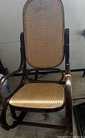 Full view of Lloyd rocking chair with visible cane seat and backrest, and dark wood frame showing scratches.