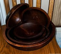 Wooden salad set stacked on a wooden chair. Set includes multiple salad bowls and plates with visible scratches and dark wood finish.