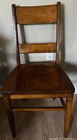 Front view of vintage wooden school chair with two horizontal slats on backrest and flat seat.