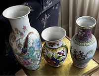 Three decorative porcelain vases placed on a table with floral and bird motifs. Includes a large Chinese ginger jar, a honey pot, and a colorful floral vase.