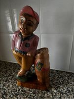 Wooden carved man figurine leaning against tree stump, painted in natural colors