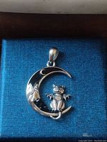 Sterling silver bat winged cat pendant on crescent moon with black tone detail shown in blue textured box.