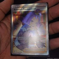 Hand-held photo of Acerola's Premonition full art holo foil Pokémon Trainer supporter card with clear visibility of holographic features and character artwork.