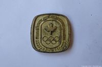 Front side of the coin with Canadian maple leaf and Olympic rings in gold tone metal