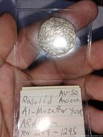 Photo of silver coin front side showing Arabic inscriptions inside decorative borders with informational card in background.