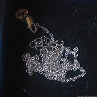 Photo of tangled sterling silver chain on a black background showing chain links and extender link.