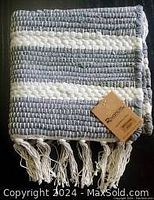 Close-up image showing detailed weave and color of the rug in grey and white with fringe tassels, along with Rivancia tag.