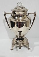 Front view of a tall shiny metallic percolator coffee urn with two handles and lid with glass knob