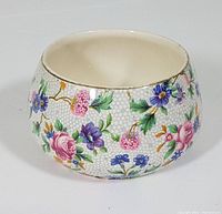 Small round cream colored ceramic bowl with Old Cottage Chintz floral pattern, showing pink roses, blue and purple flowers, and gold rim.