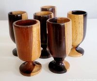 Front view of six two-tone teak wood goblets standing upright showing the contrasting wood colors and rounded base.