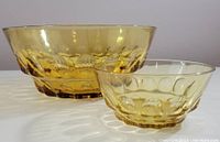 Two amber glass bowls, large and small, set on a white surface with light casting their patterns.