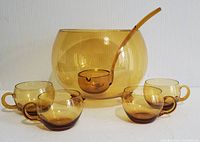 Full set of amber blown crystal punch bowl, four cups, and ladle displayed on white surface against neutral background.