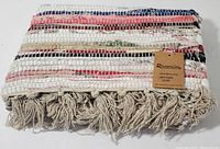 Folded hand woven cotton rug showing multicolor weave and fringe edges with Rivancia tag