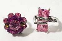 Two vintage costume jewelry rings on white background, featuring pink rhinestones in different styles, one with large rectangular stone and the other a cluster of smaller stones.