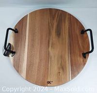Top view of round acacia wood serving board with two black metal handles secured to opposite sides, showing natural wood grain.