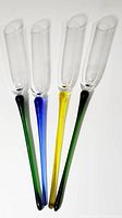 Four hand blown champagne toasting flutes laid out, showing colorful long stems in deep green, cobalt blue and yellow, with clear glass bowls at top.