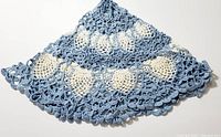 Photo showing blue and cream colored handcrafted crocheted table accent with visible scalloped edges and intricate lacework
