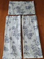 Photo showing two navy and white toile curtain panels, laid flat on wooden floor, side by side with top hem rod pocket visible.