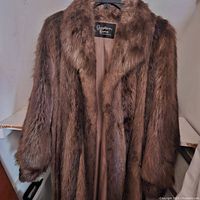 Photo of full length longhaired beaver fur coat, front view, showing natural brown fur with dense texture, open to show inside lining and label.