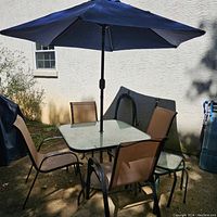 Full view of square glass-top table with umbrella installed, surrounded by four sling chairs on concrete patio