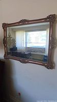 Large rectangular mirror showing ornate pink-gold carved frame mounted on wall near window.