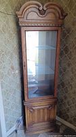 Front view of antique wooden cabinet with glass shelves behind a glass door showing overall structure and carved top.