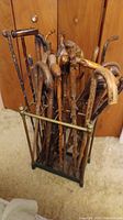 Multiple wooden antique canes with different shaped handles held upright in metal cane holder, showing natural wood wear and variety