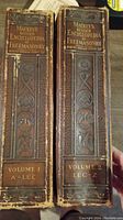 Spines of two leather-bound volumes labeled Mackey's Revised Encyclopedia of Freemasonry, Volume 1 (A-LEC) and Volume 2 (LEC-Z), showing embossed Masonic symbols and author Robert Ingham Clegg 33°. The spines are worn at edges.