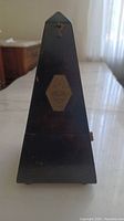 Front view of antique metronome showing its traditional pyramid shape and brass plate