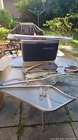 Table with vintage fish nets, blue cooler, folded umbrella, hanging scales, horse shoes, and fishing pliers.