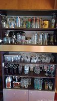 Wide view of the cabinet showing shelves filled with assorted bar glasses, cocktail shaker, and coaster holder.
