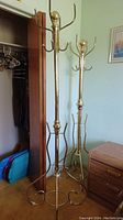 Two brass-colored clothes racks standing next to each other in a room showing overall height and design details.